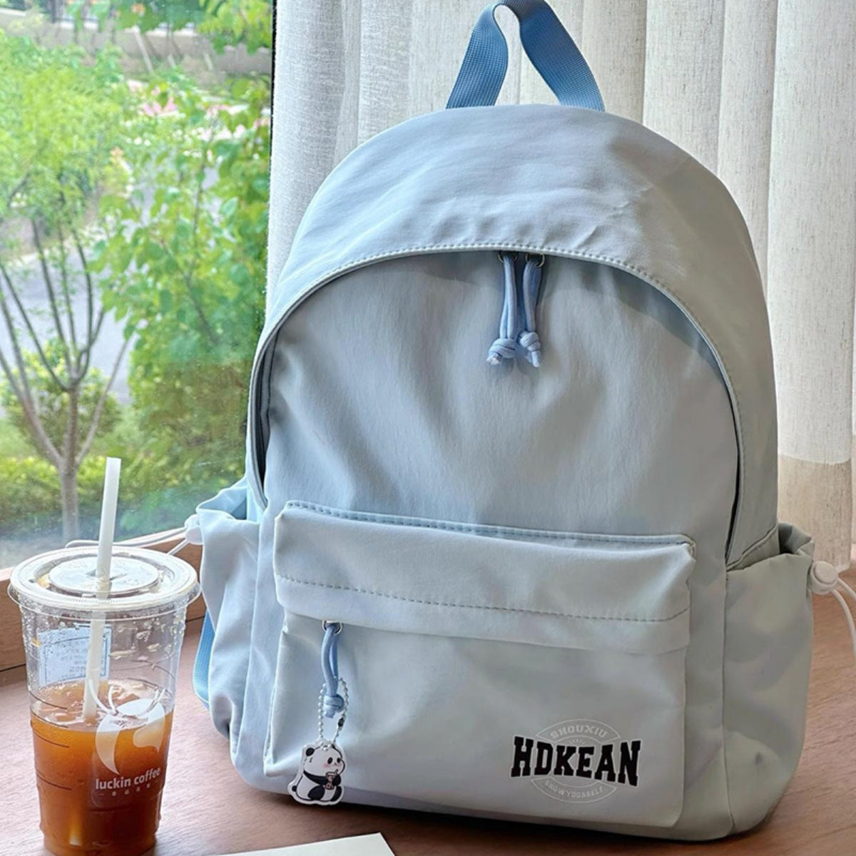 Blue nylon backpack with front pocket, drawstring closure, and panda charm.