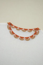 White knit sweater with a scalloped neckline featuring a floral pattern in orange and tan.