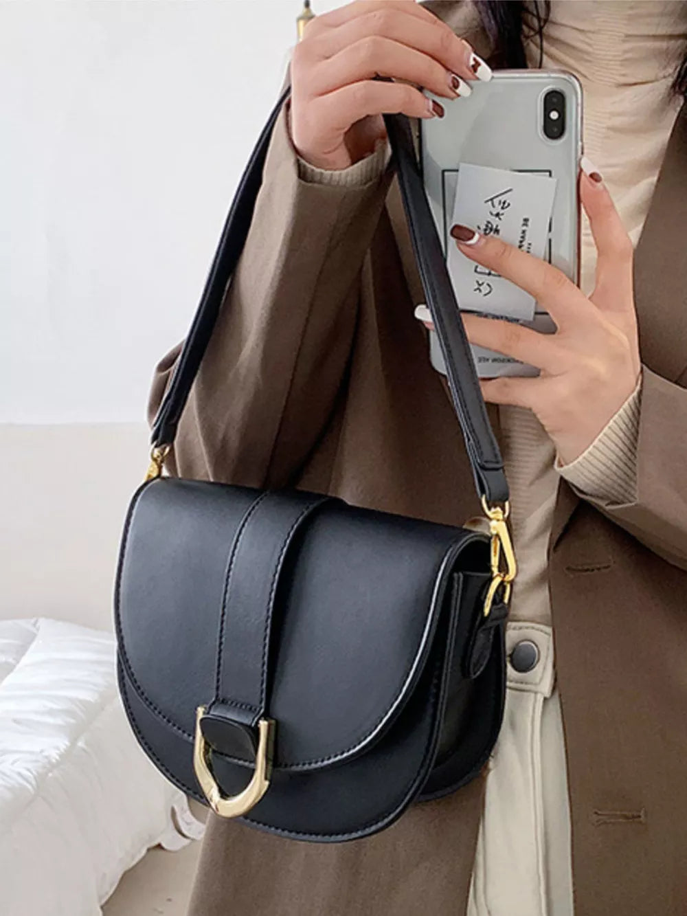 Chic black semi-circular flap crossbody bag with gold hardware and adjustable strap.