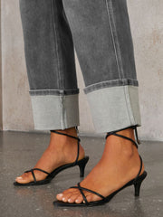Dark wash denim jeans with wide legs and large cuffs, styled with black strappy kitten heels.