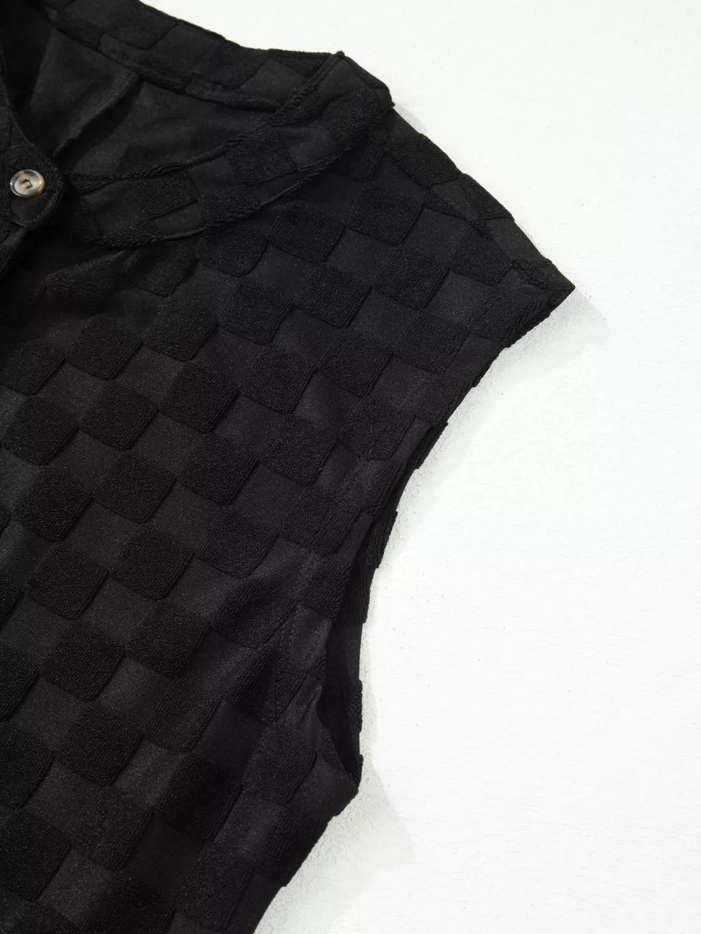 Black textured checkered button-down jumpsuit with collared neckline and short sleeves.