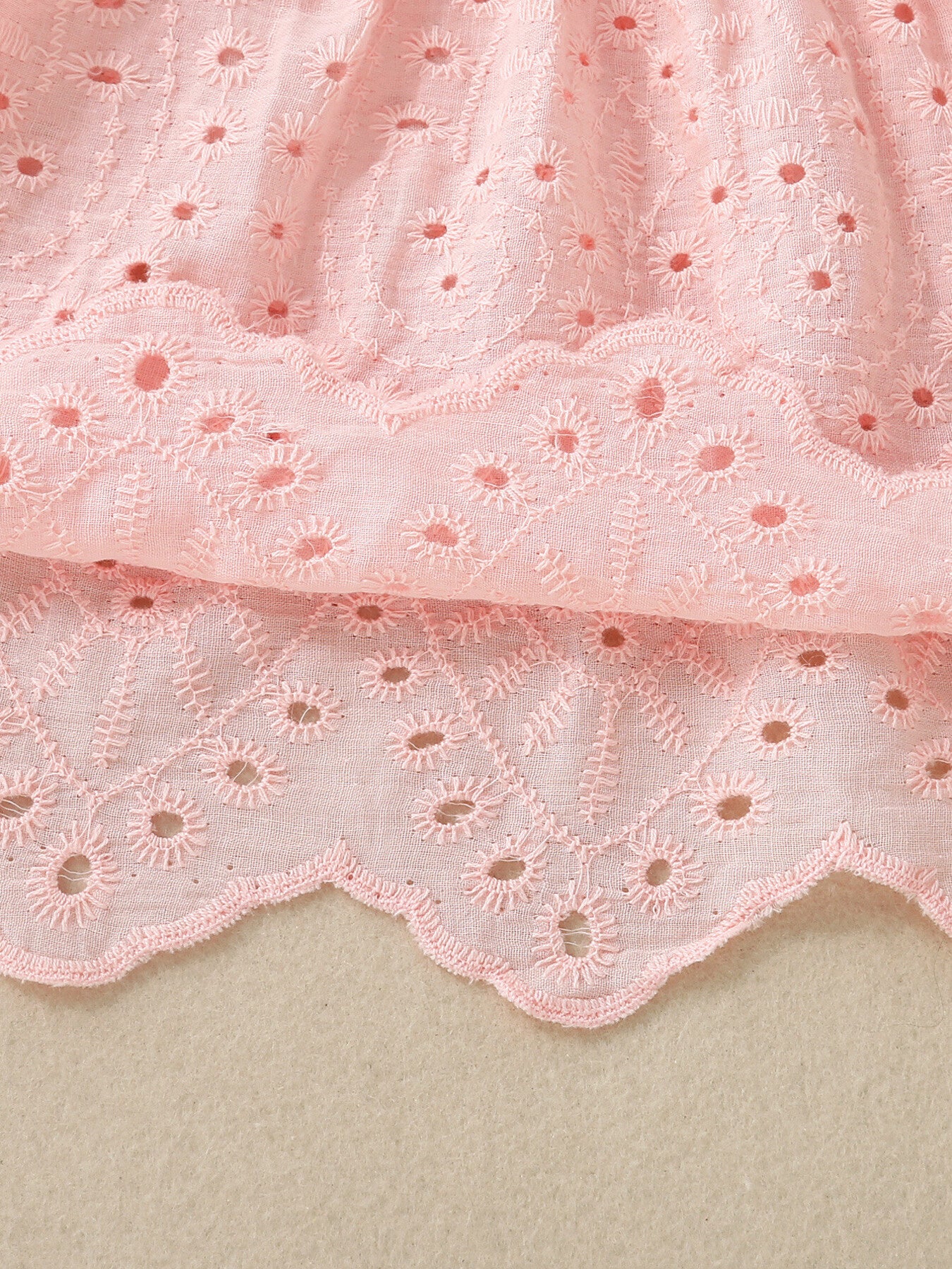 Pink cotton baby top with eyelet embroidery and scalloped hem detail.