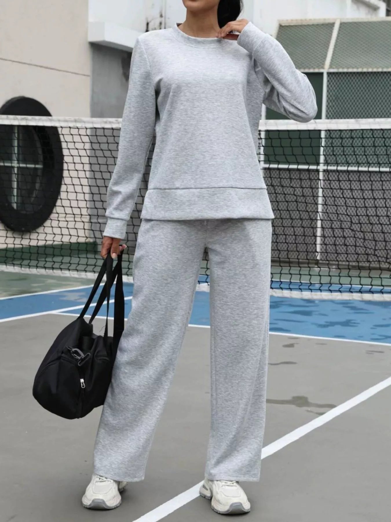 Light gray sweat set with crewneck sweatshirt and wide-leg joggers, styled with a black duffel bag.