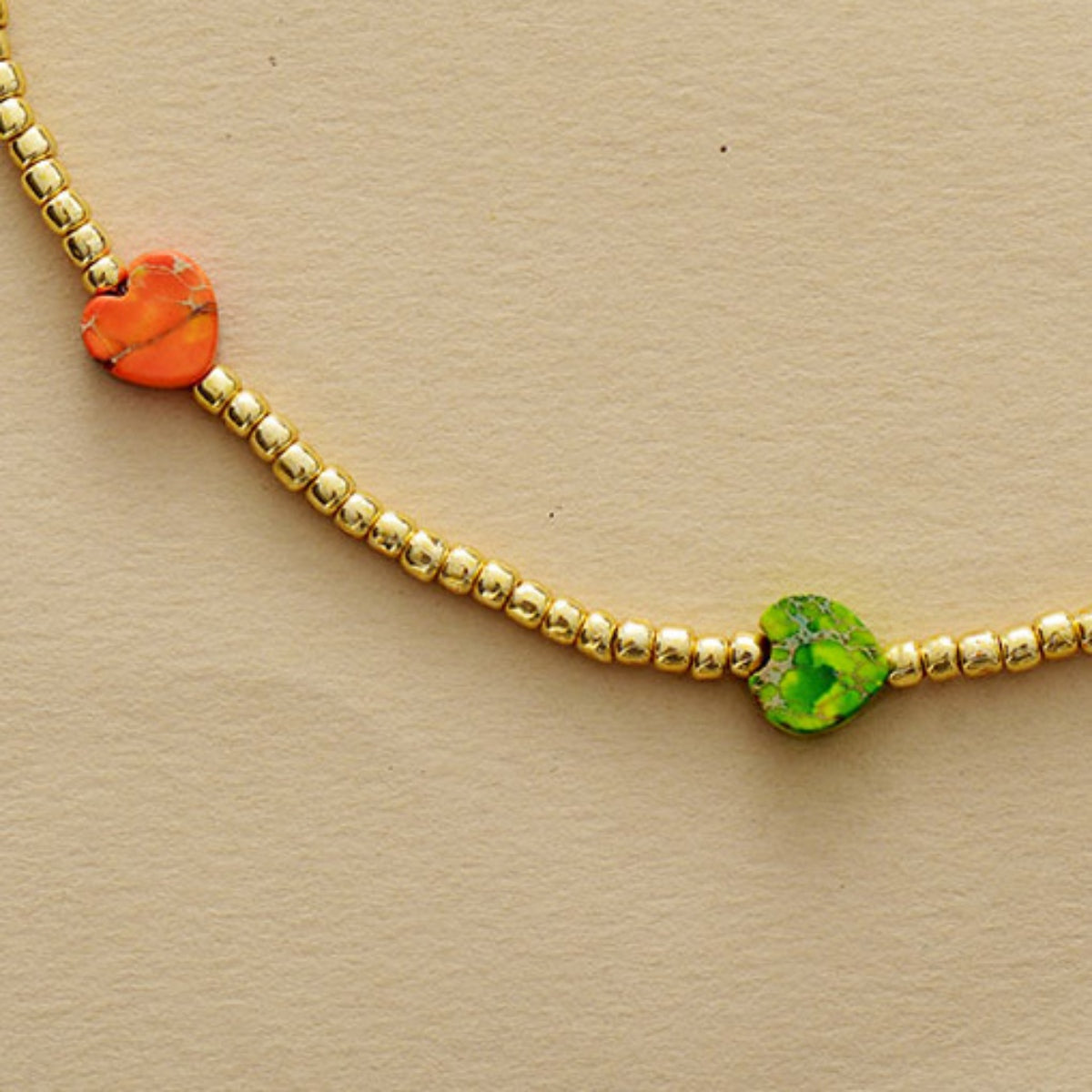 Gold beaded necklace with orange and green heart charms