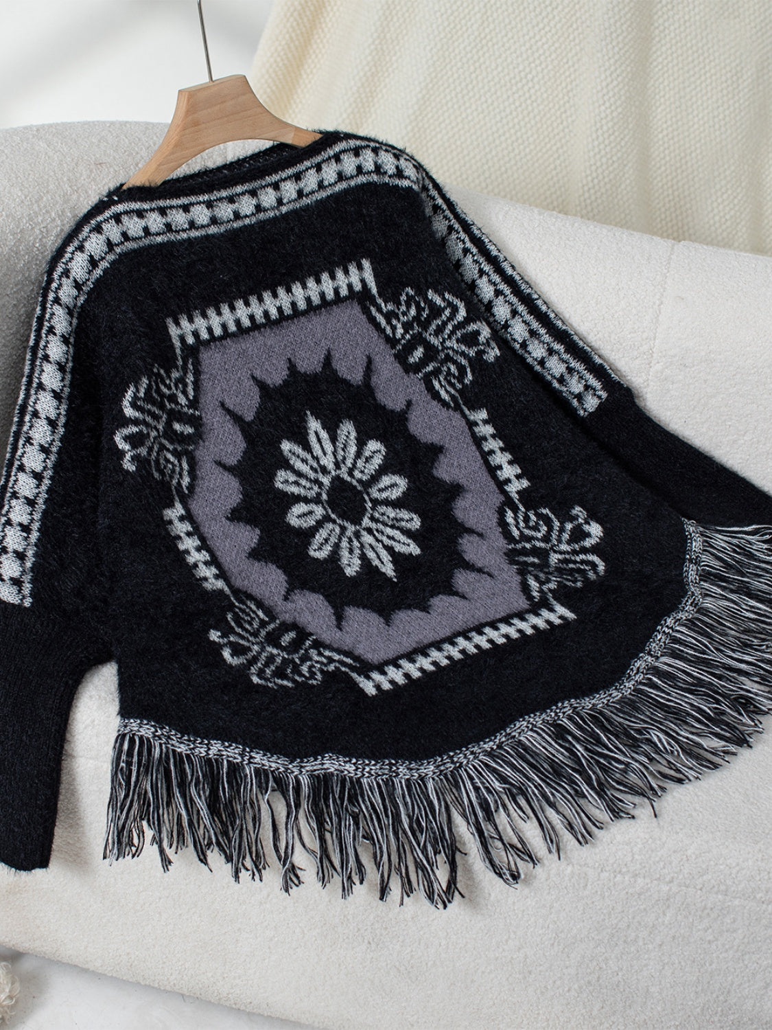 Black acrylic poncho with Aztec motif, fringe hem, and crew neck.