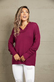 Burgundy textured knit hooded pullover sweater with fringe trim and long sleeves.