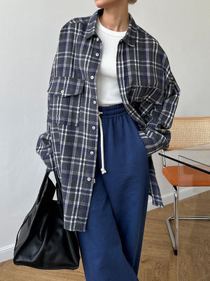 Plaid button-up shacket with chest pockets in dark navy and grey, worn open over a white top.