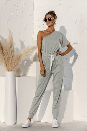 Gray asymmetric sweat jumpsuit with drawstring waist and cuffed jogger legs.