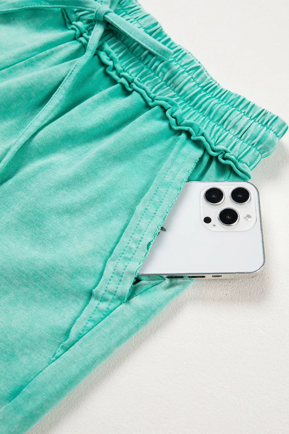Mineral washed cotton shorts in green with drawstring waist and ruffled elastic detail, showing a phone in the pocket.