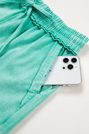 Mineral washed cotton shorts in green with drawstring waist and ruffled elastic detail, showing a phone in the pocket.