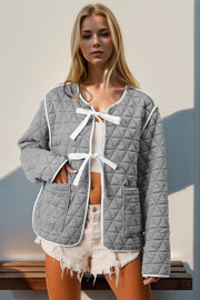 Diamond quilted jacket in gray with white trim and bow closure.