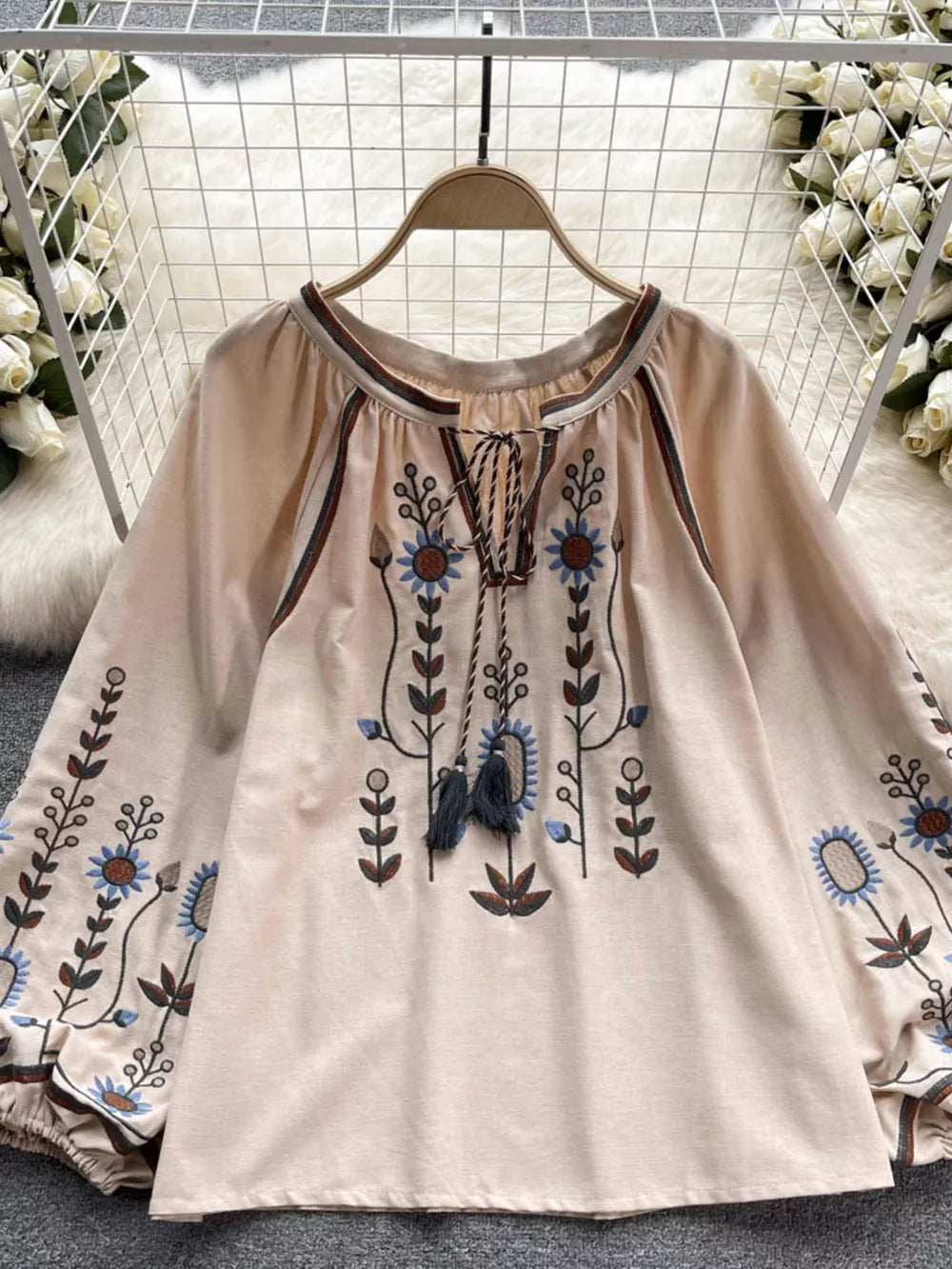 Apricot tie neck blouse with intricate floral embroidery and billowy sleeves.