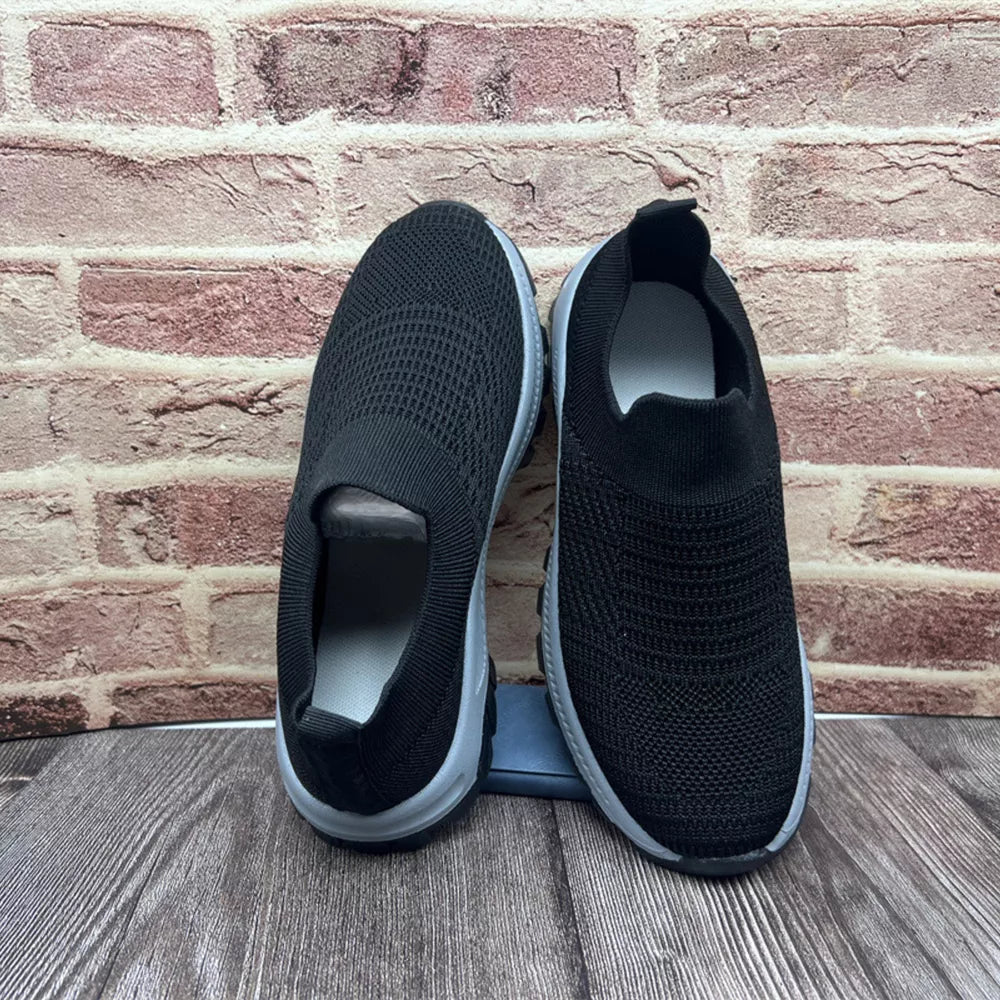 Black breathable round toe slip-on sneakers with a knit upper and grey sole.