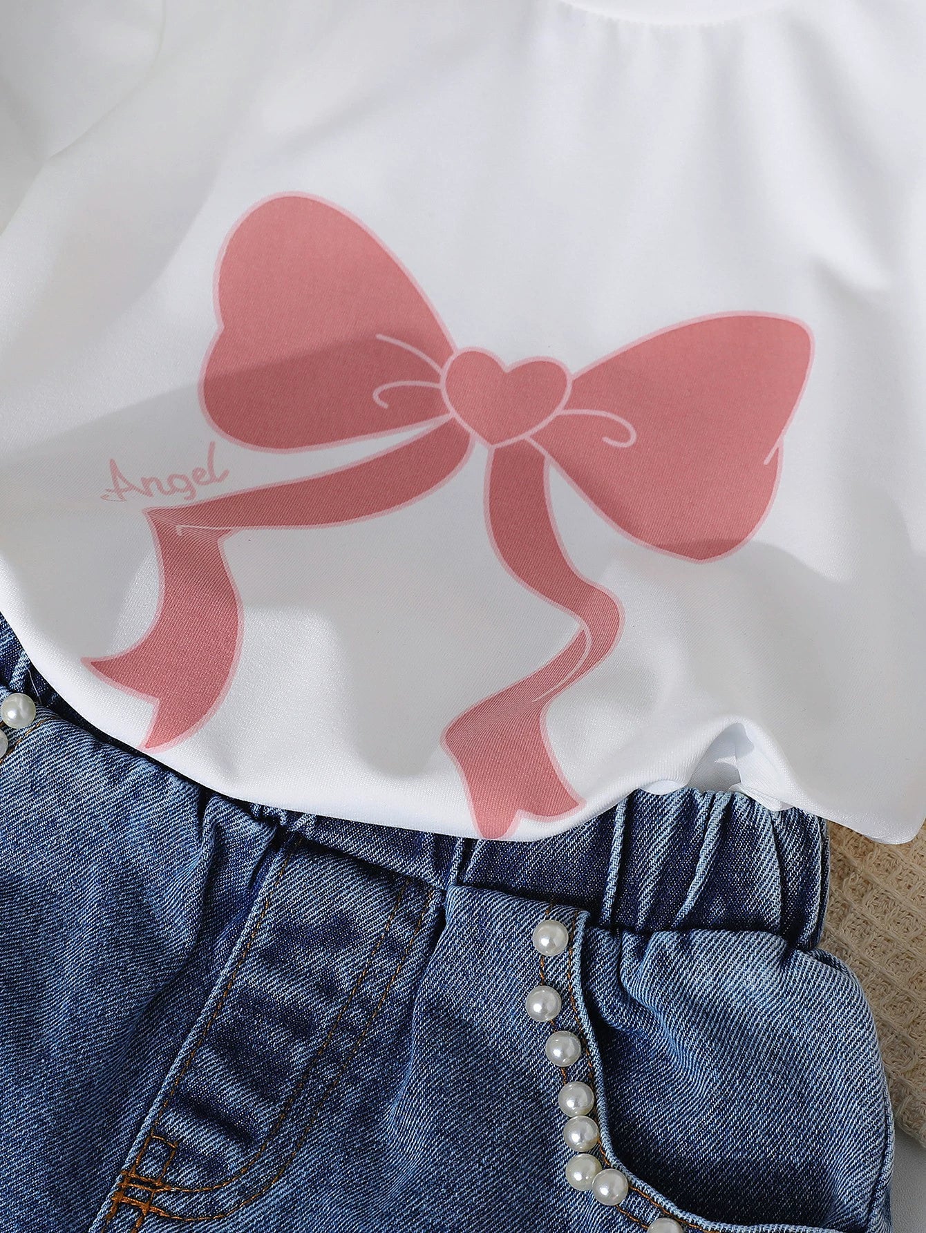 White tee with pink bow print and pearl-trimmed denim shorts.