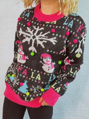 Black knit sweater with snowflake, snowman, and "Fa la la" print, embellished with colorful pom-poms.