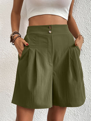 Pleated front bermuda shorts in dark green with button closure and textured fabric.