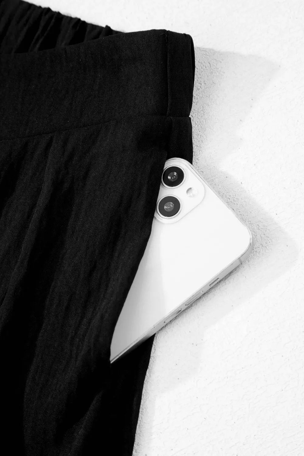 Black textured maternity pants with wide legs and a crossed waist detail, showing a phone in the pocket.