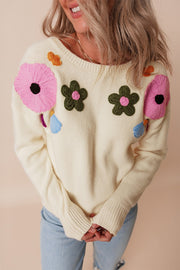 Cream knit sweater with embroidered floral appliqués and tassels.