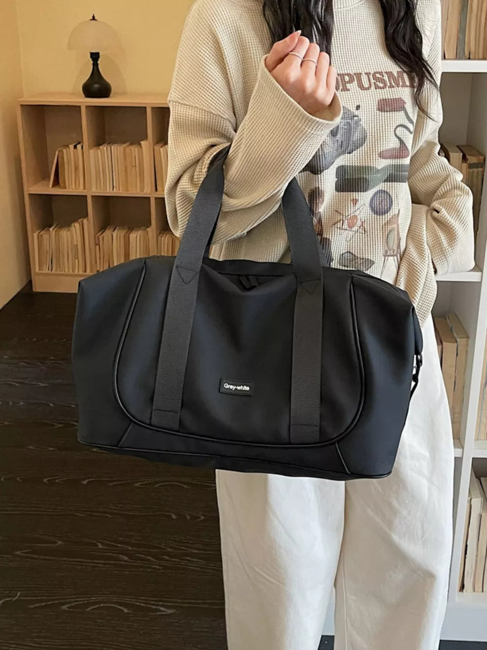 Black nylon travel duffle bag with curved stitching and adjustable strap.