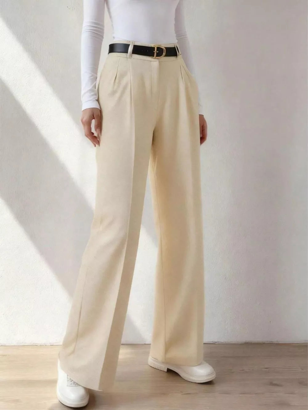 Beige wide-leg dress pants with pockets, belt loops, and a pleated front, styled with a black belt.