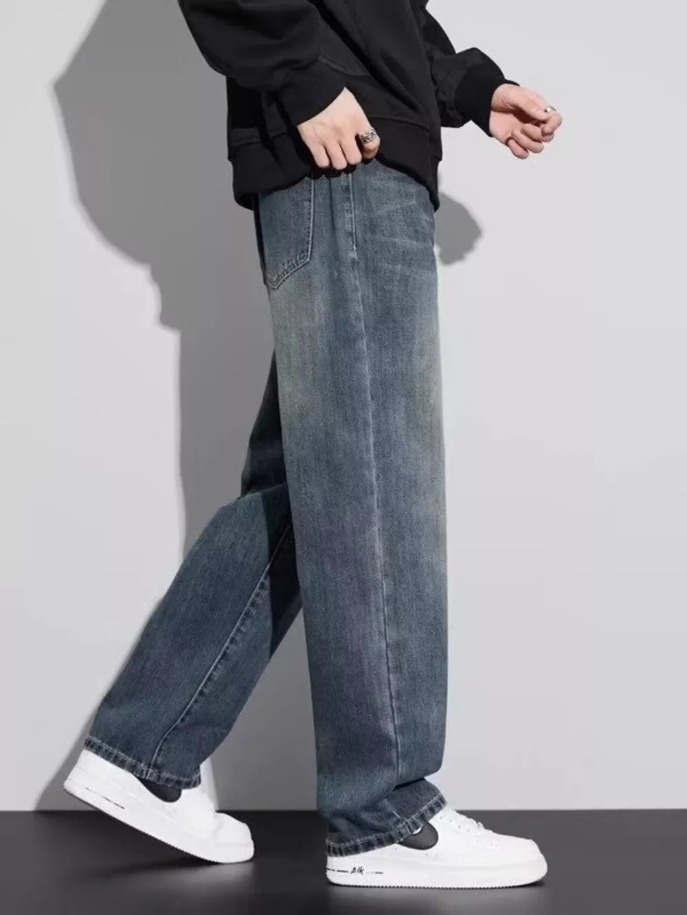 Men's vintage wash relaxed fit jeans in blue cotton, shown with a black hoodie and white sneakers.