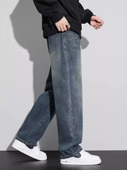 Men's vintage wash relaxed fit jeans in blue cotton, shown with a black hoodie and white sneakers.
