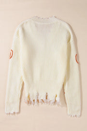 Beige distressed knit sweater with orange pumpkin patches on sleeves and frayed hem.