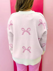 Beige drop shoulder sweater with all-over pink bow print, crew neck, and ribbed hem.