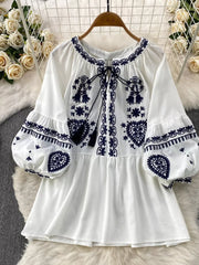 White tie-neck blouse with intricate blue embroidery and balloon sleeves.