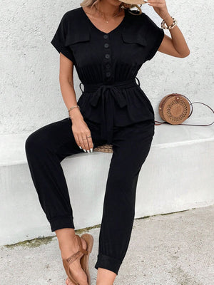 Black utility jumpsuit with tie waist, button front, V-neck, short sleeves, and chest pockets.