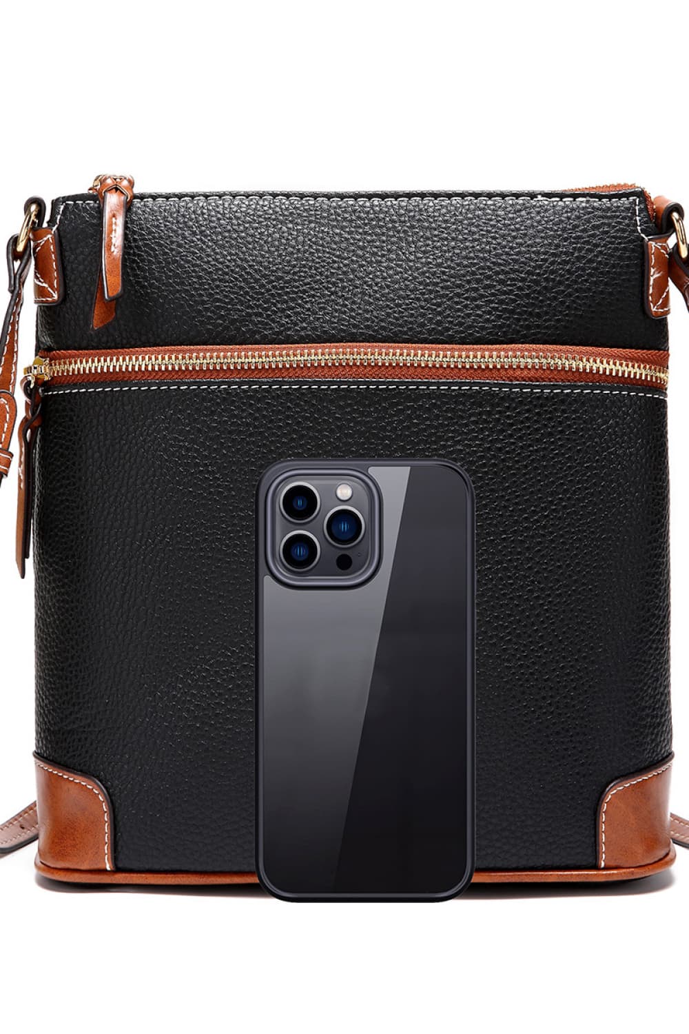 Black leather crossbody bag with brown trim and white stitching, featuring a top zipper and a phone for scale.