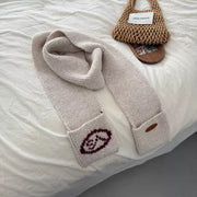 Off-white textured knit scarf with pockets and maroon logo detail.