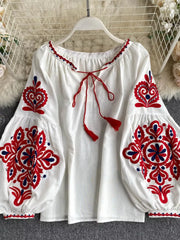 White peasant blouse with red and blue embroidery, tie neck, and tassel details.