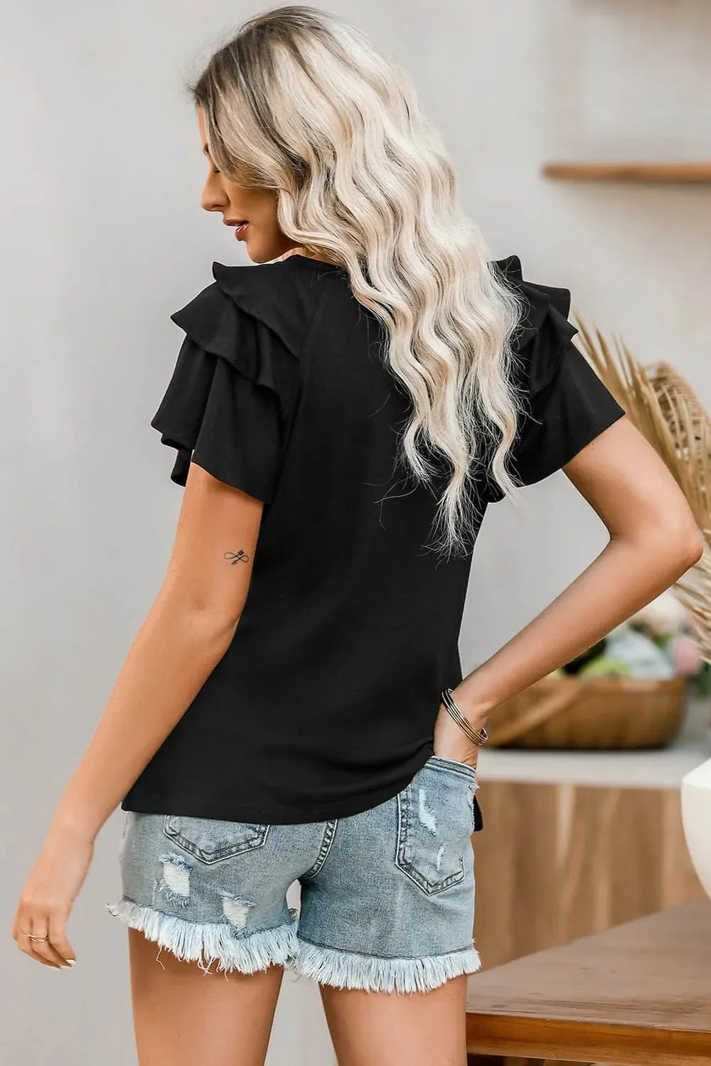 Black t-shirt with ruffle sleeves and a graphic print, styled with distressed denim shorts.