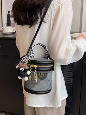 Quilted mini bucket bag in gray with black trim, checkered scarf detail, and fuzzy charm.