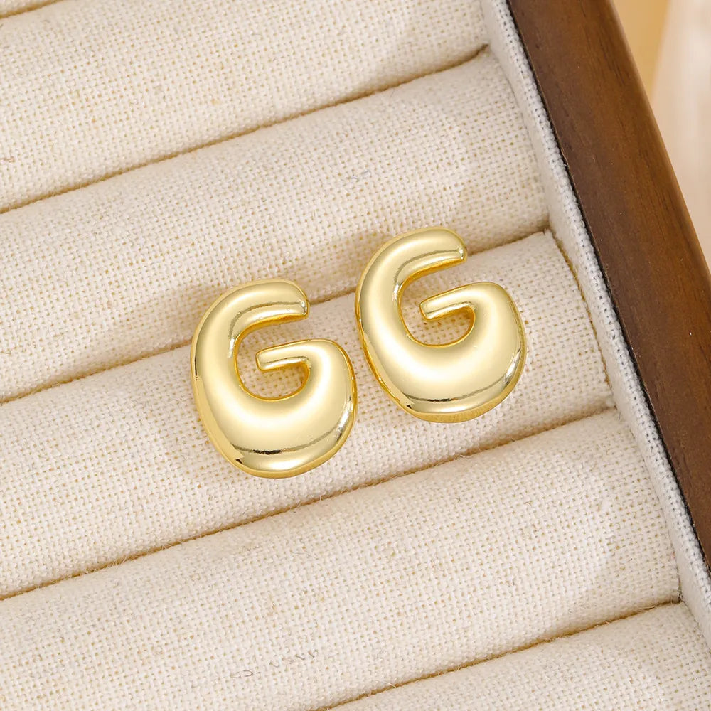 Gold sculptural stud earrings in the shape of the letter G.