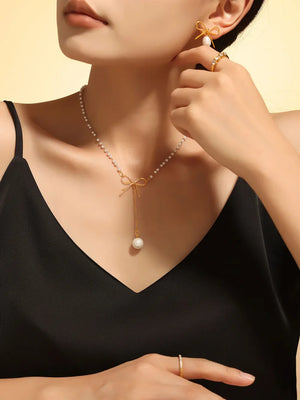 Gold pearl lariat necklace with bow detail and single pearl drop.