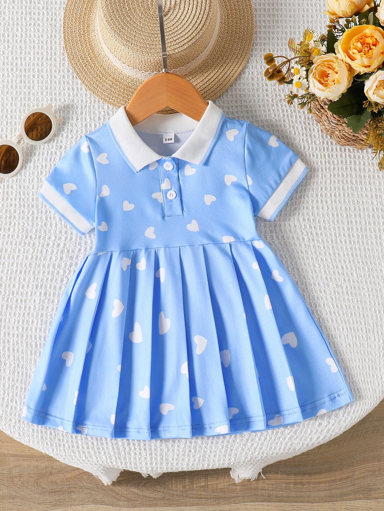 Baby dress with white hearts on blue, white collar, short sleeves, and pleated skirt.