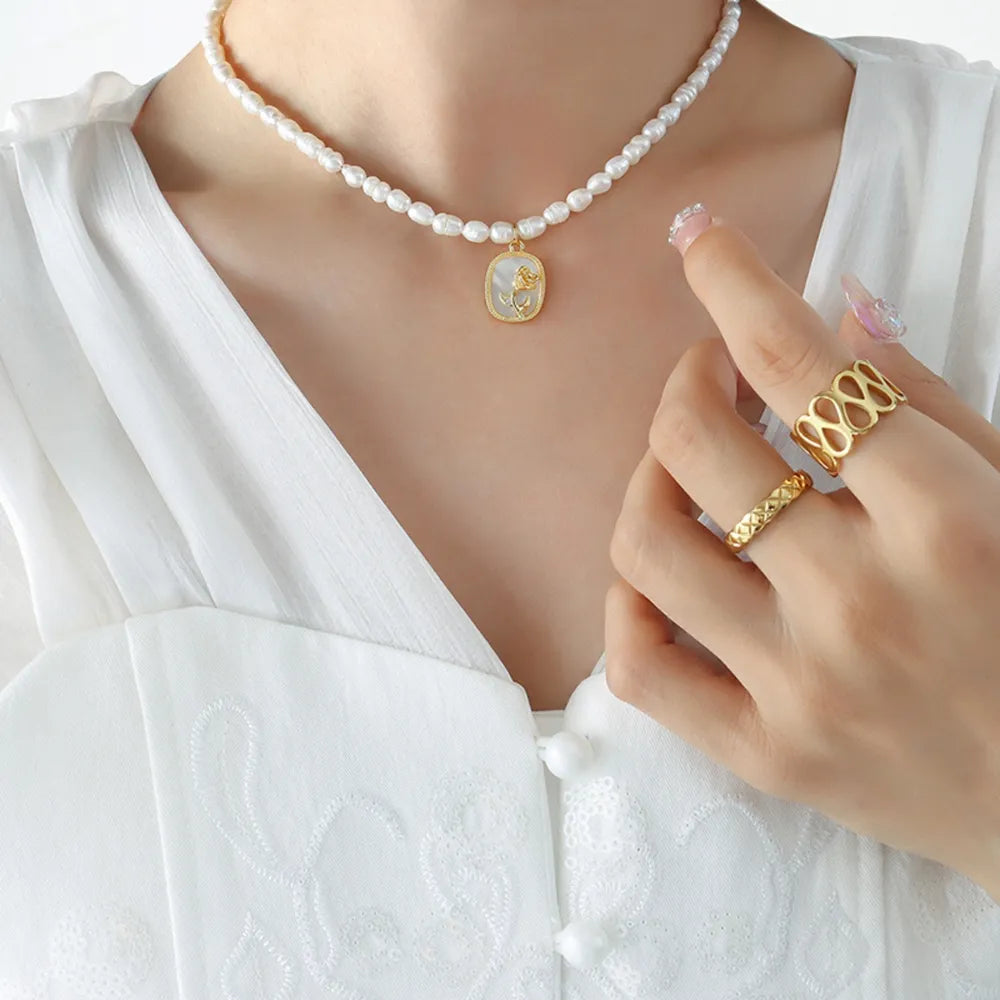 Gold baroque pearl necklace with floral medallion pendant and gold rings.