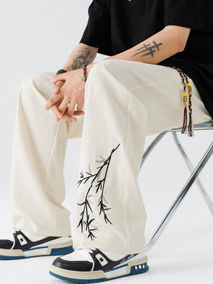 Beige wide-leg sweatpants with embroidered branch detail on left leg.
