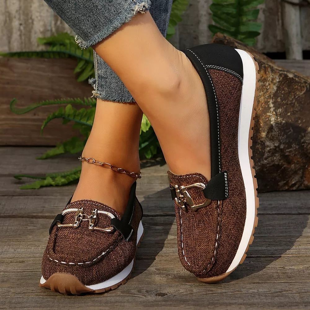 Brown round toe slip-on loafers with buckle detail and white stitching.