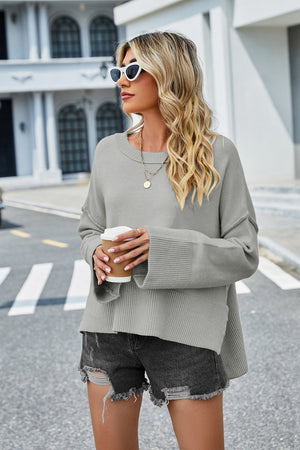 Grey acrylic knit sweater with flared sleeves and slit hem detail.