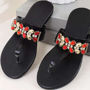 Black jeweled toe-post flat sandals with red and gold embellishments.