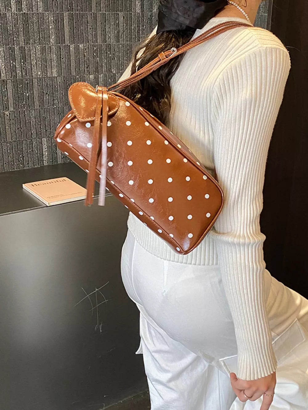 Brown polka dot shoulder bag with heart detail and tassels, worn casually.