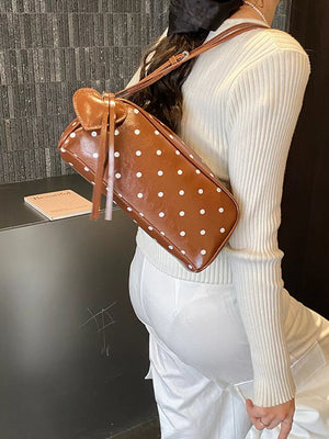 Brown polka dot shoulder bag with heart detail and tassels, worn casually.