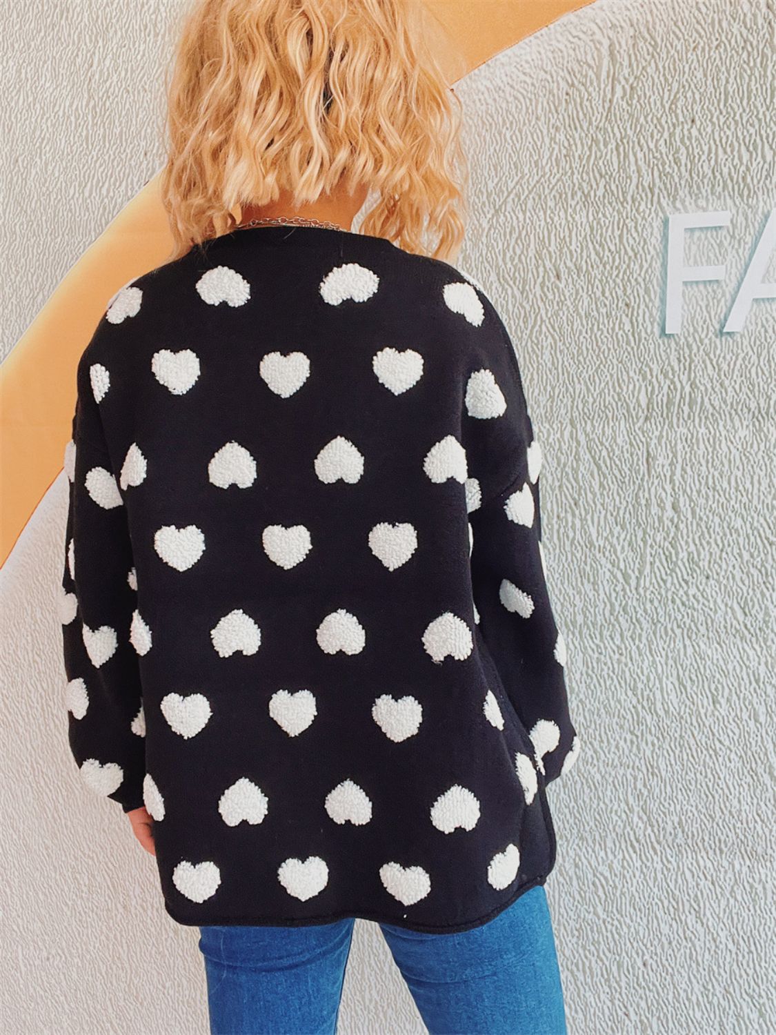 Black acrylic cardigan with white textured heart motif pattern, crew neck, long sleeves.