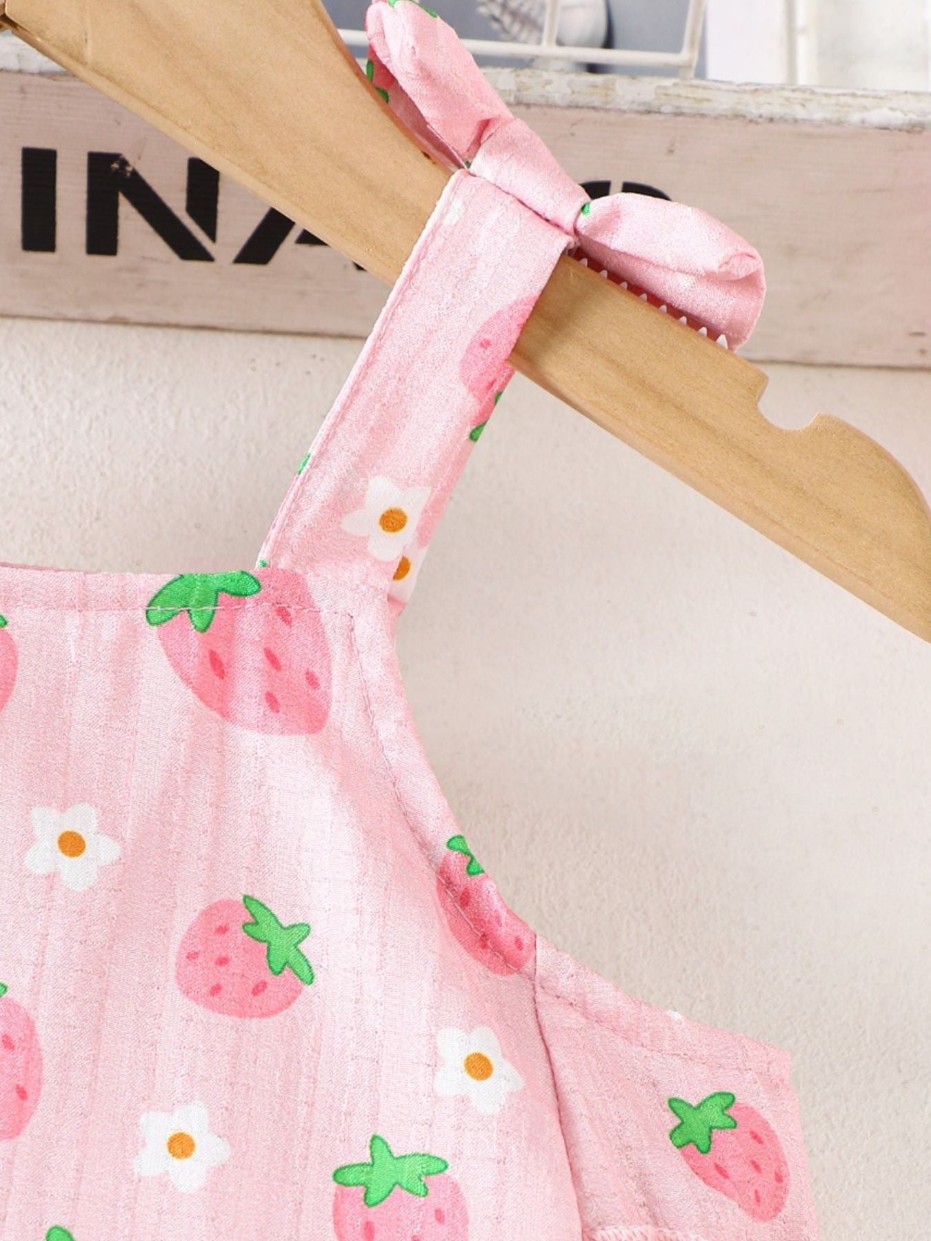Pink strawberry print cami with tie straps and white flowers.