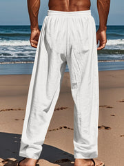 White relaxed fit drawstring sweatpants with button-fly, cotton blend, on a man at the beach.