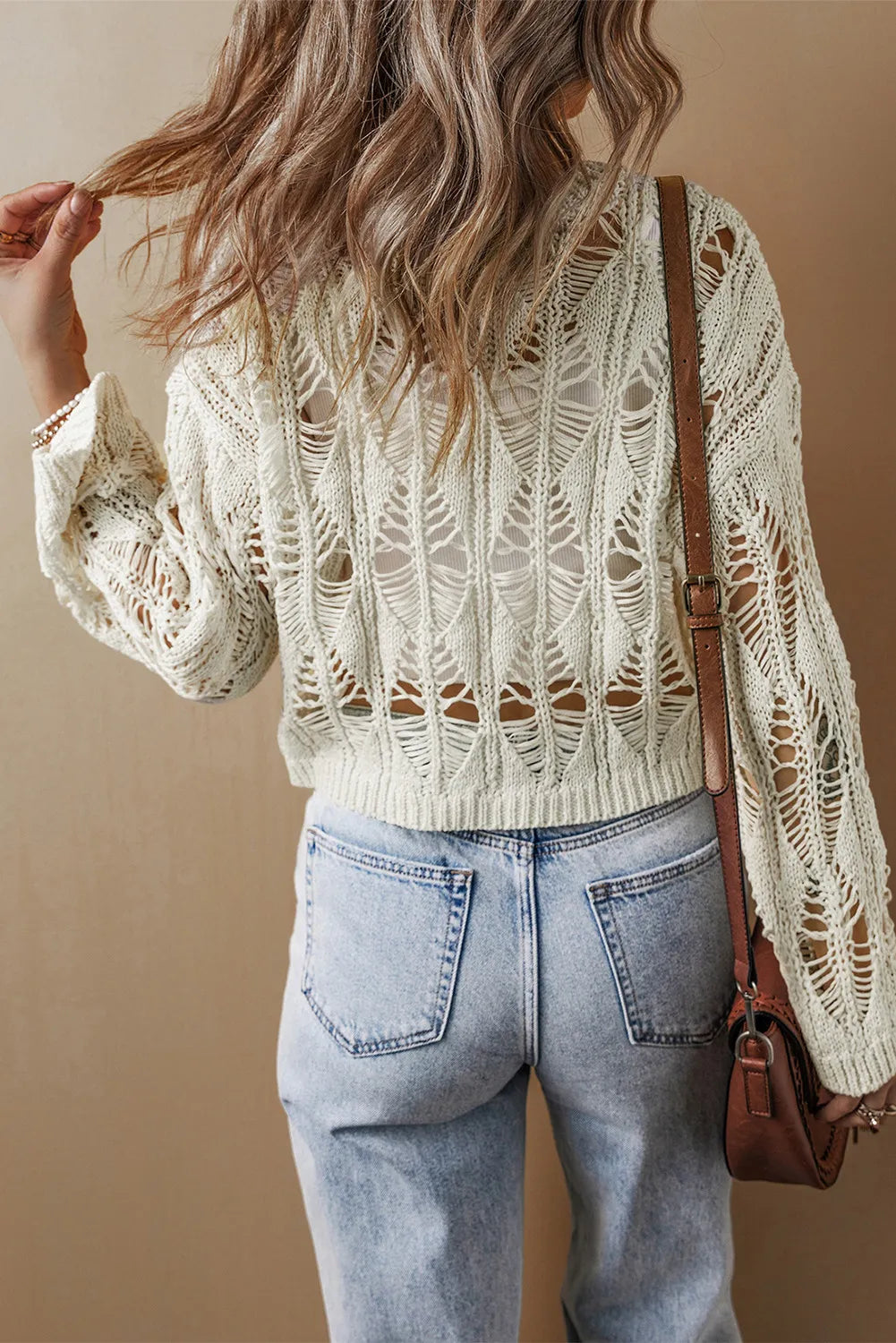 Ivory open-knit crochet crop sweater with distressed details and long sleeves.