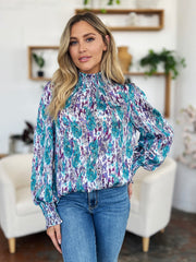 High neck abstract print blouse in blue and red-violet with smocked cuffs and neckline.